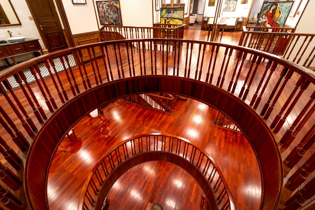 A beautiful wooden spiral staircase in an art gallery with vibrant paintings and polished floors. Un magnifique escalier en colimaçon en bois dans une galerie d'art avec des peintures vibrantes et des sols polis.