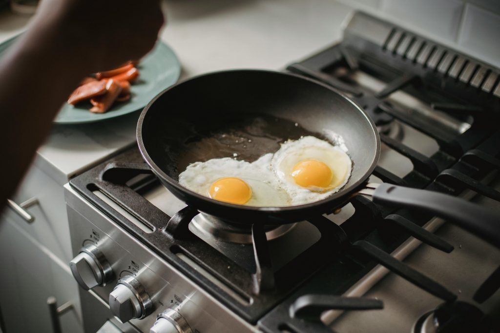 Close-up de deux œufs au plat cuisant dans une poêle sur une plaque de cuisson moderne.