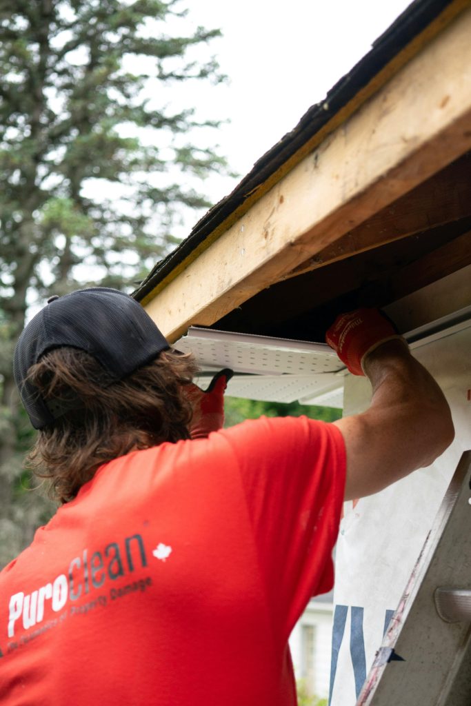 Un ouvrier du bâtiment en chemise rouge installe une gouttière sous un toit en bois, en se concentrant sur la précision.