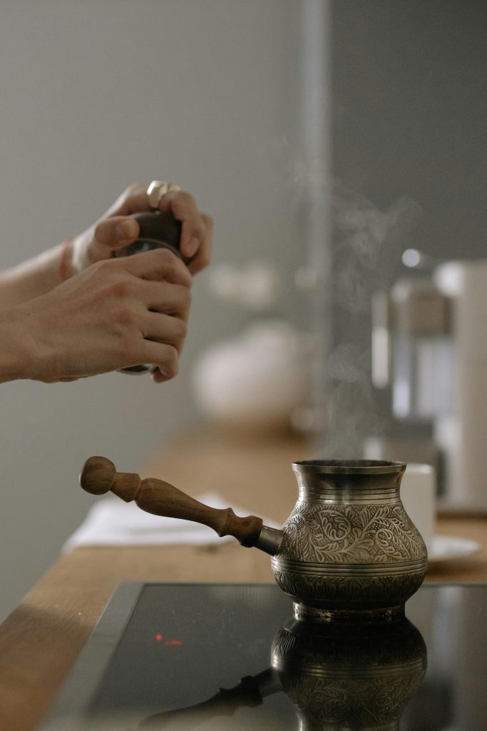 Mains préparant du café avec une cezve sur une plaque à induction, montrant de la vapeur et des méthodes traditionnelles.