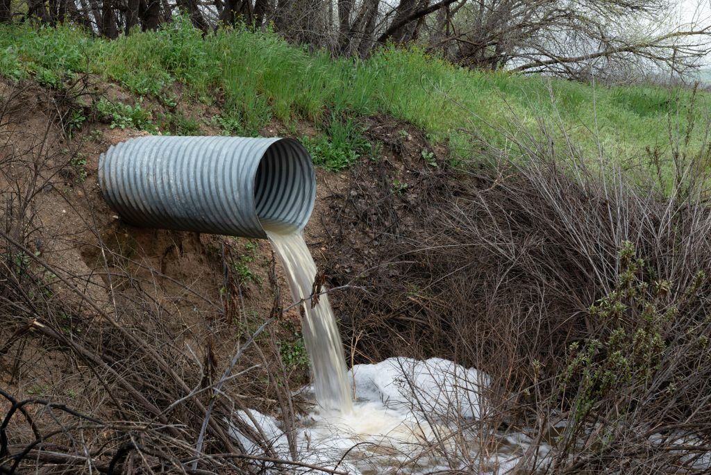 Un tuyau de drainage rural déversant de l'eau dans un ravin naturel, entouré de végétation verte.