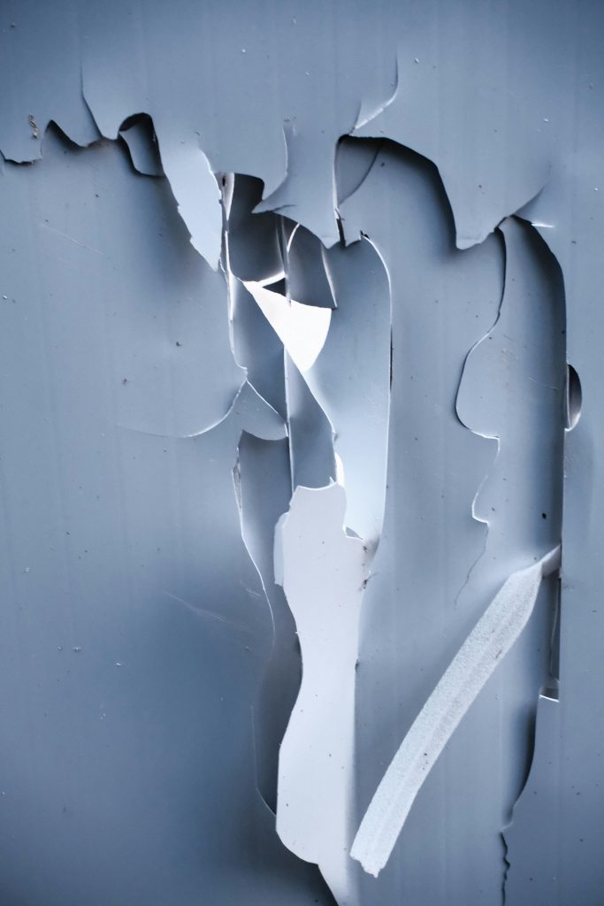 Écaillage de peinture bleue en gros plan révélant la texture sous-jacente, créant des motifs abstraits.