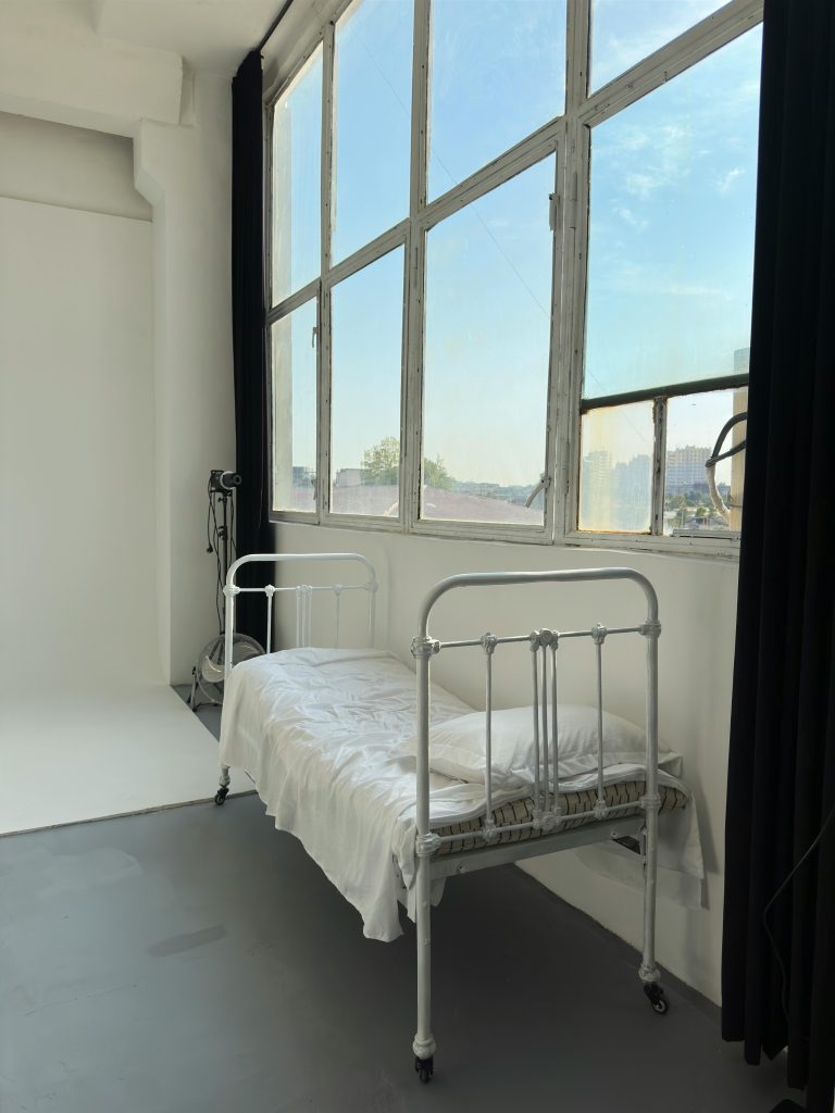 Bright, minimalist room featuring a vintage metal bed by large windows. Pièce minimaliste lumineuse avec un lit en métal vintage près de grandes fenêtres.