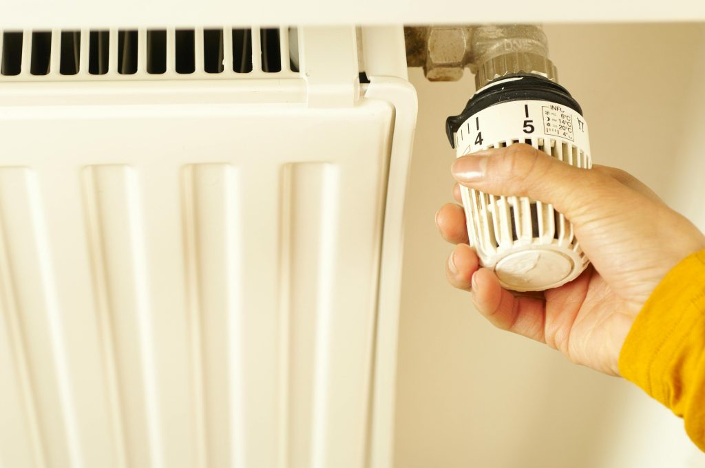 Gros plan d'une main ajustant un thermostat de radiateur pour contrôler la température de chauffage à la maison.