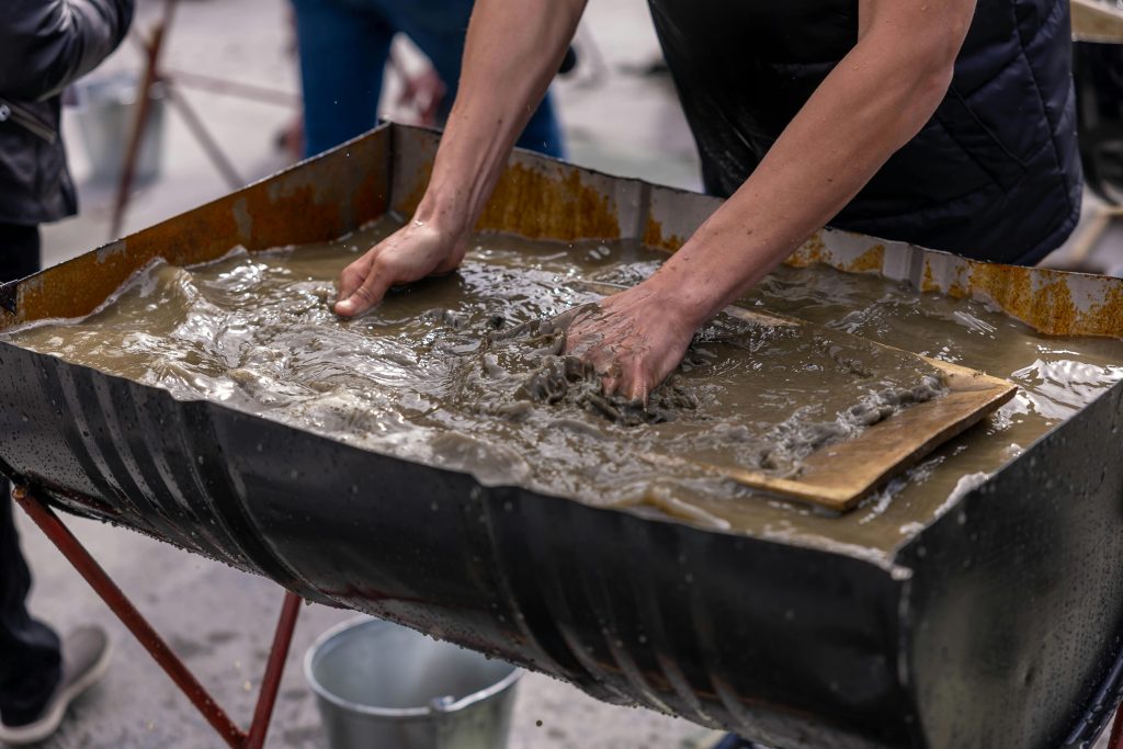 Mains mélangeant du coulis de béton dans un grand récipient pour des travaux de construction en extérieur.
