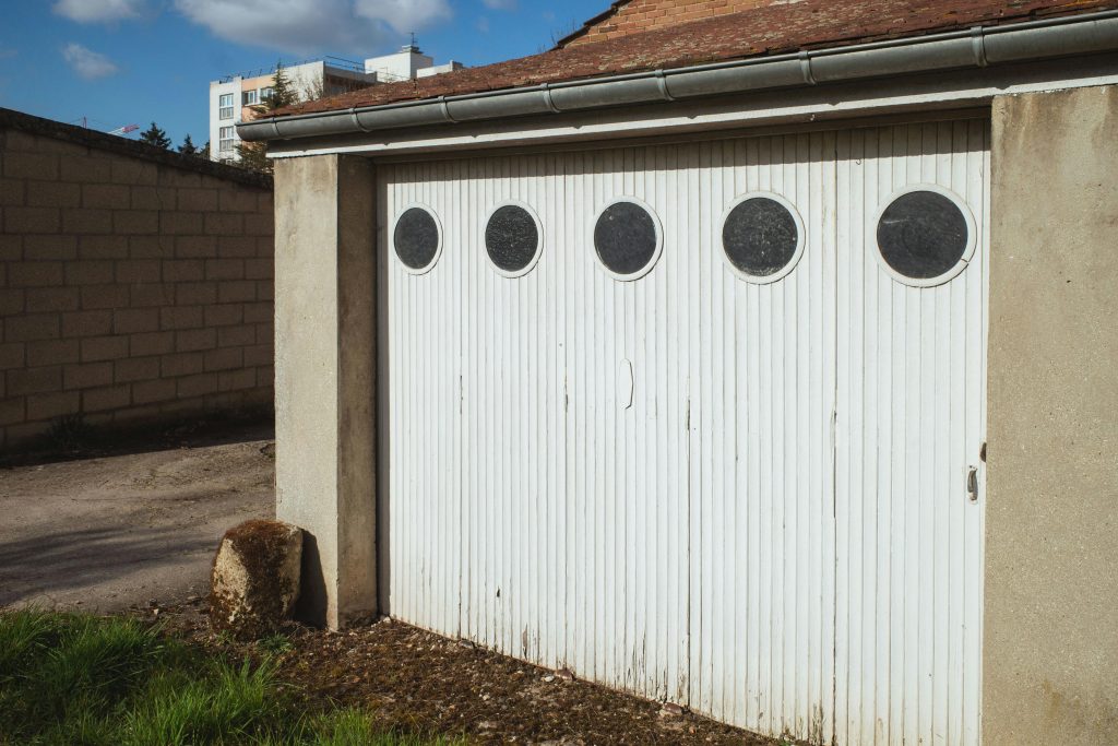 Porte de garage blanche avec des fenêtres circulaires dans un quartier résidentiel de Compiègne, France.