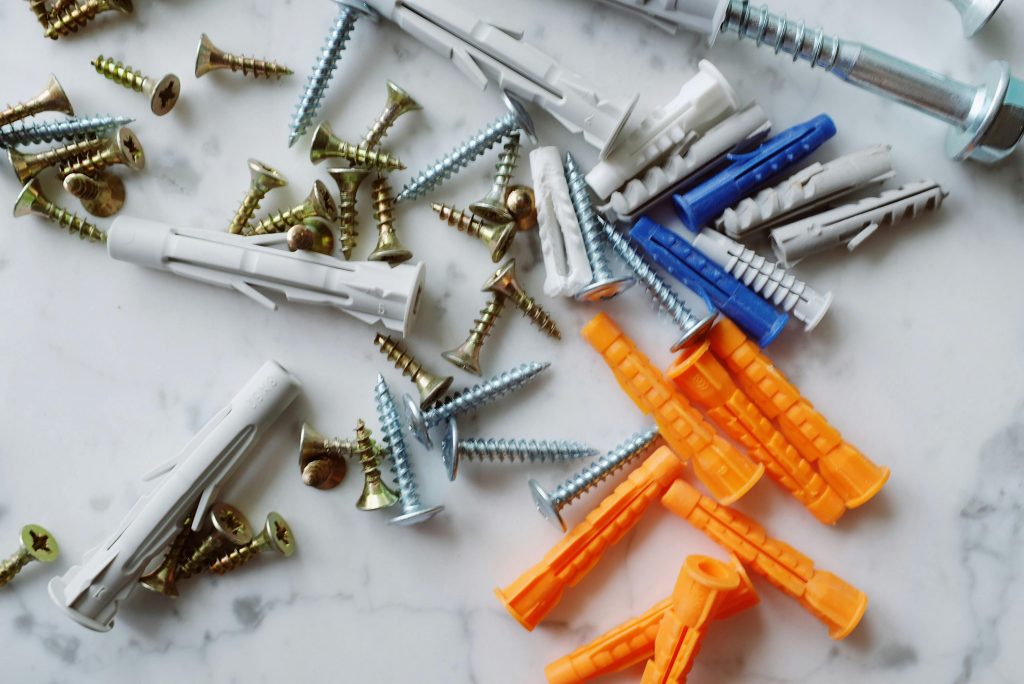 Set of various multicolored plastic dowels with assorted metal screws of different sizes placed on white marble table in modern workshop Ensemble de chevilles en plastique multicolores de diverses tailles avec des vis en métal assorties de différentes tailles placées sur une table en marbre blanc dans un atelier moderne.