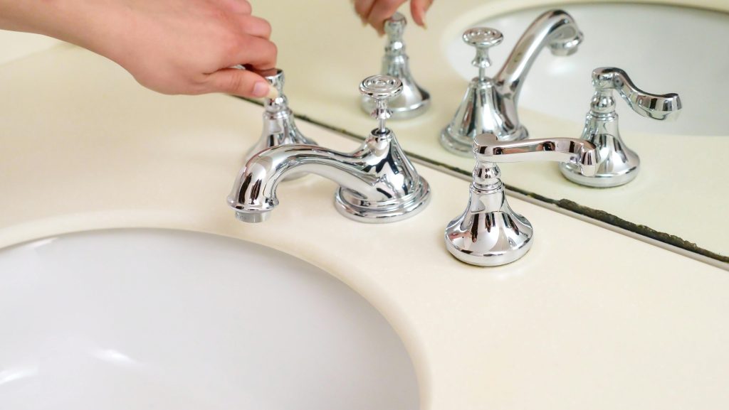 Close-up of a hand adjusting a chrome faucet in a modern bathroom interior. Gros plan d'une main ajustant un robinet chromé dans l'intérieur d'une salle de bain moderne.