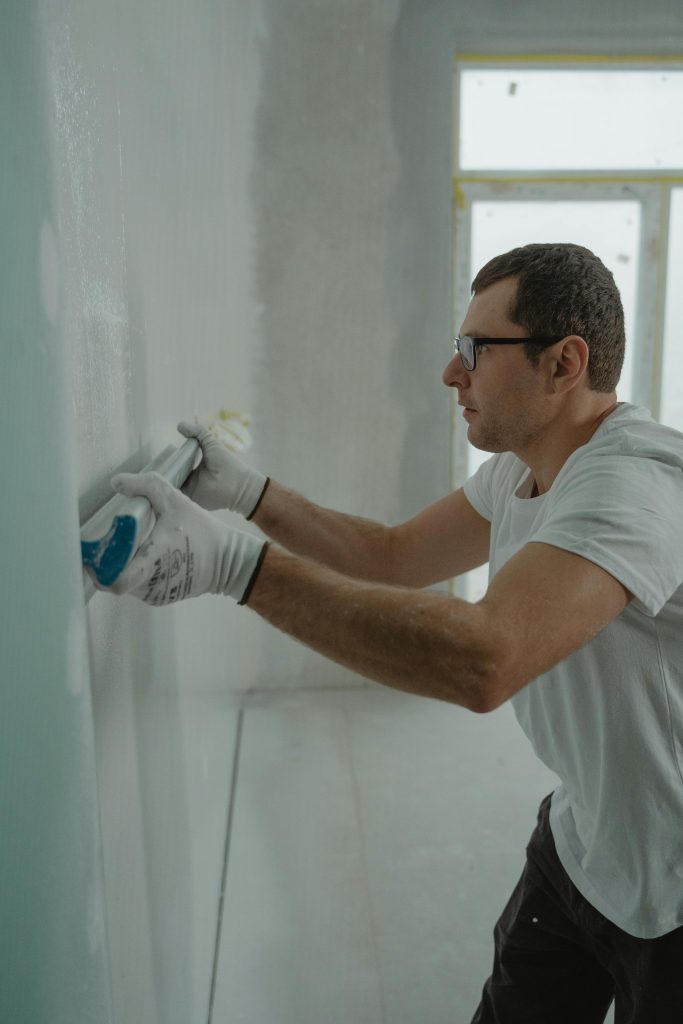 A focused worker applying drywall compound during a home renovation project indoors. Un ouvrier concentré appliquant du composé de cloison sèche lors d'un projet de rénovation domiciliaire à l'intérieur.