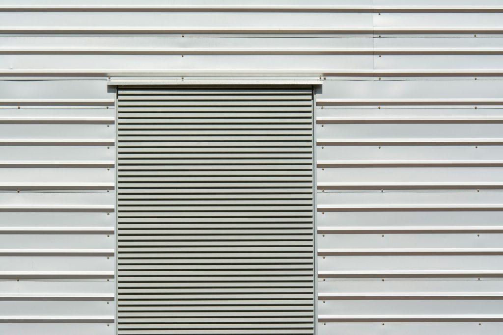 Close-up of a minimalist metal rolling door on a white sheet metal wall, ideal for industrial themes. Gros plan d'une porte roulante en métal minimaliste sur un mur en tôle blanche, idéale pour les thèmes industriels.