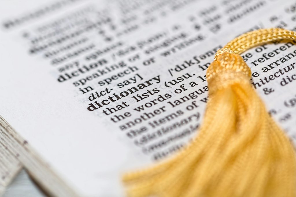 Close-up image of a dictionary page focused on the word 'dictionary' with a yellow tassel. Gros plan d'une page de dictionnaire mettant l'accent sur le mot « dictionnaire » avec un gland jaune.