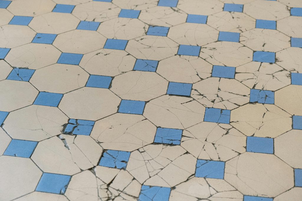 A detailed view of aged cracked tiles with a blue and white geometric pattern. Une vue détaillée de carreaux fissurés vieillis avec un motif géométrique bleu et blanc.