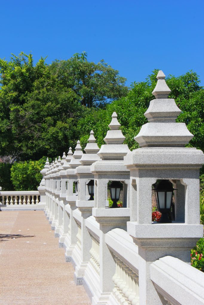 A line of ornate stone balustrades with lanterns in a sunny outdoor garden setting. Une rangée de balustrades en pierre ornementées avec des lanternes dans un cadre de jardin extérieur ensoleillé.