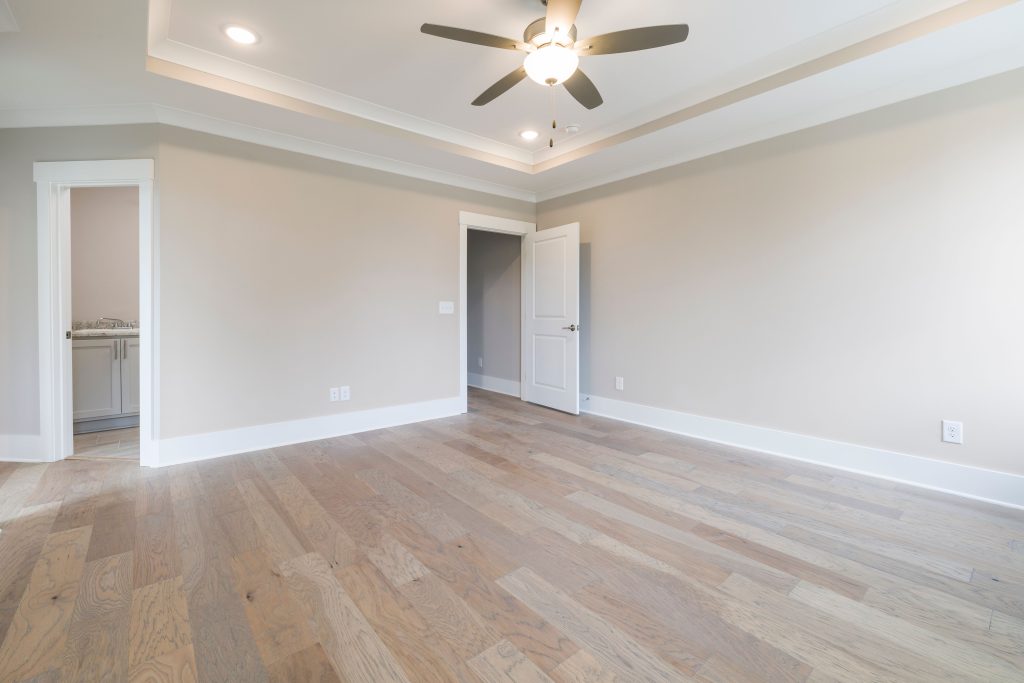 Pièce vide et lumineuse avec sols en bois, ventilateur de plafond et portes ouvertes.