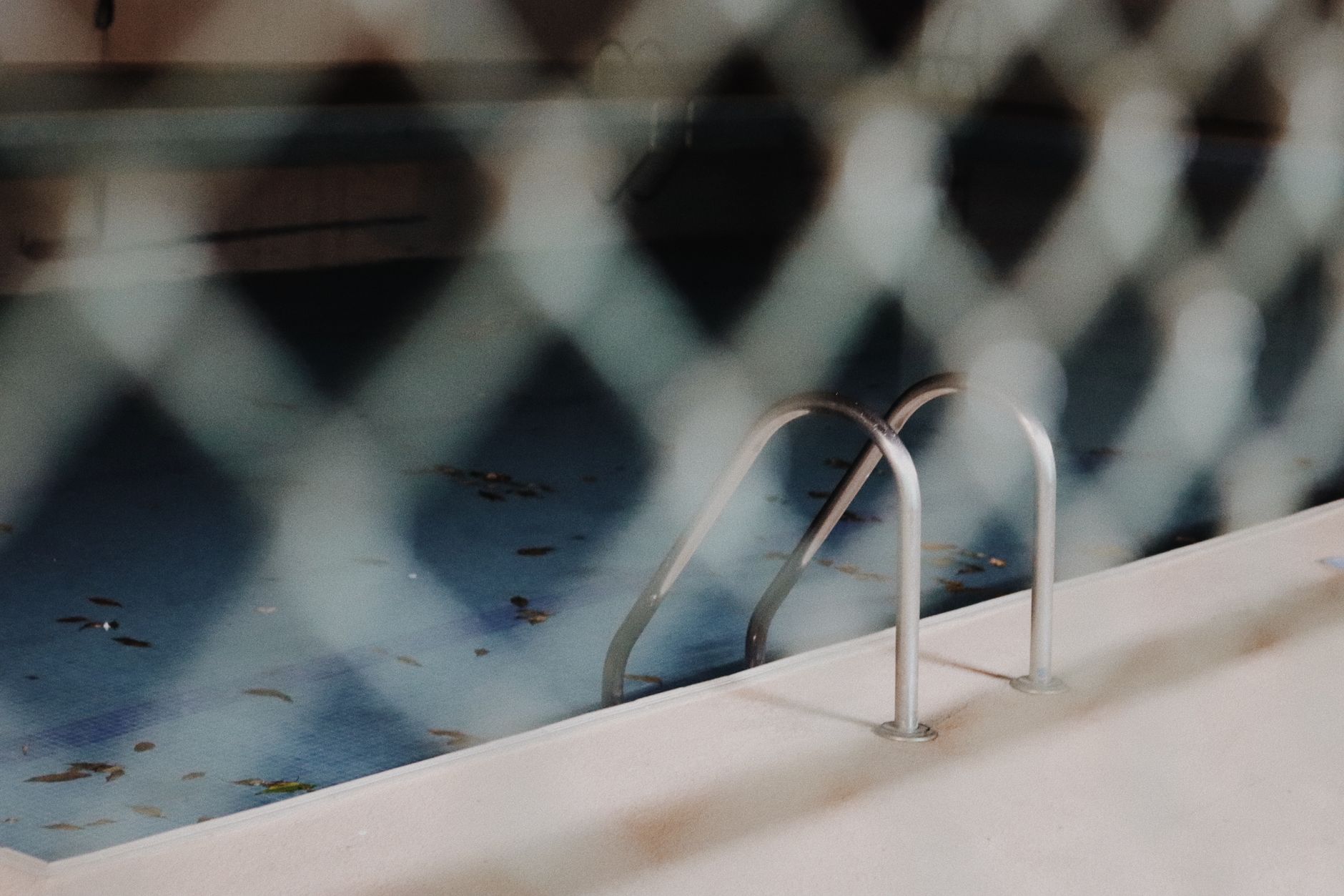 Piscine à l'abandon avec une eau trouble vue à travers un grillage