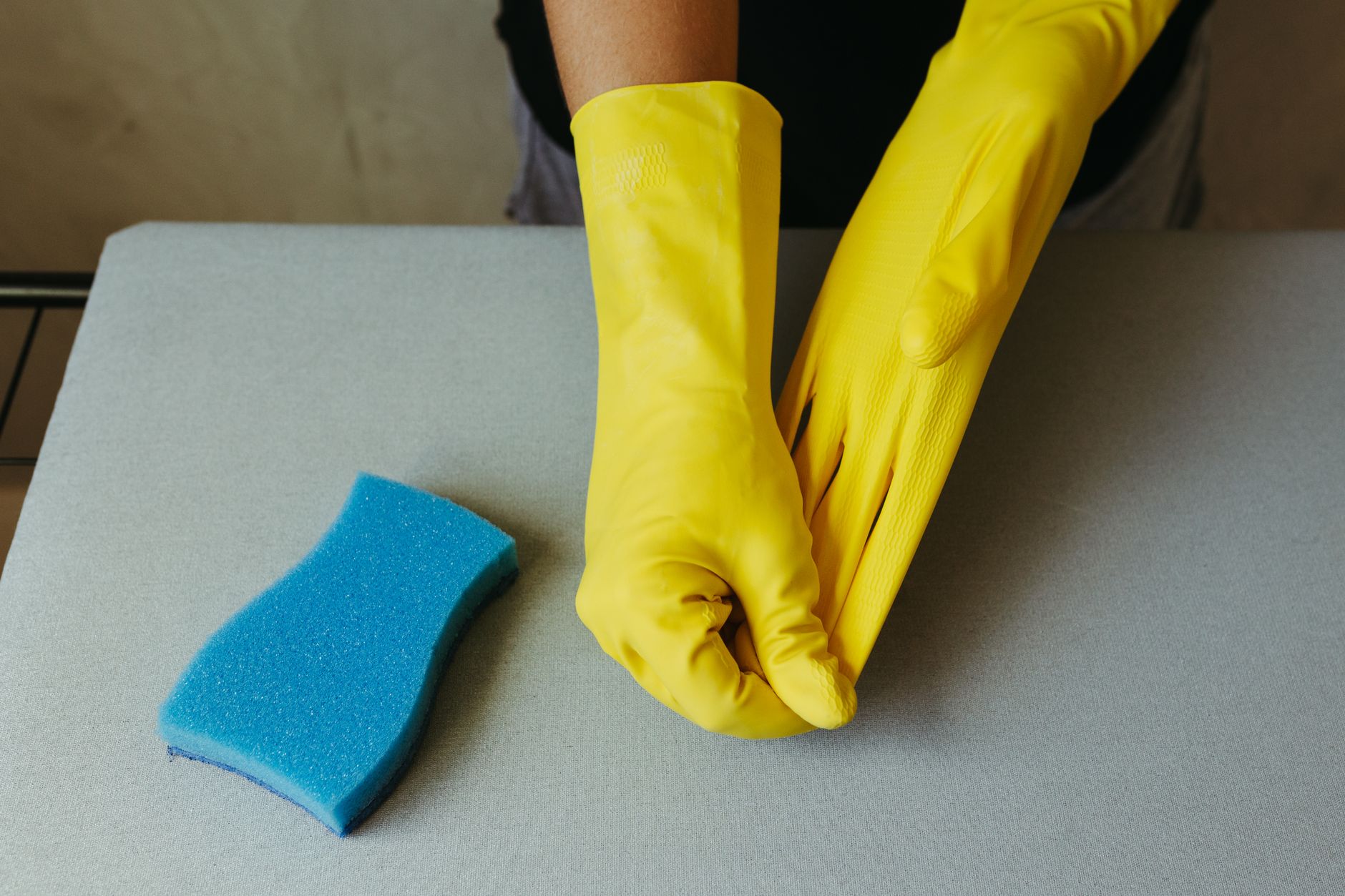 Mains gantées de caoutchouc jaune près d’une éponge