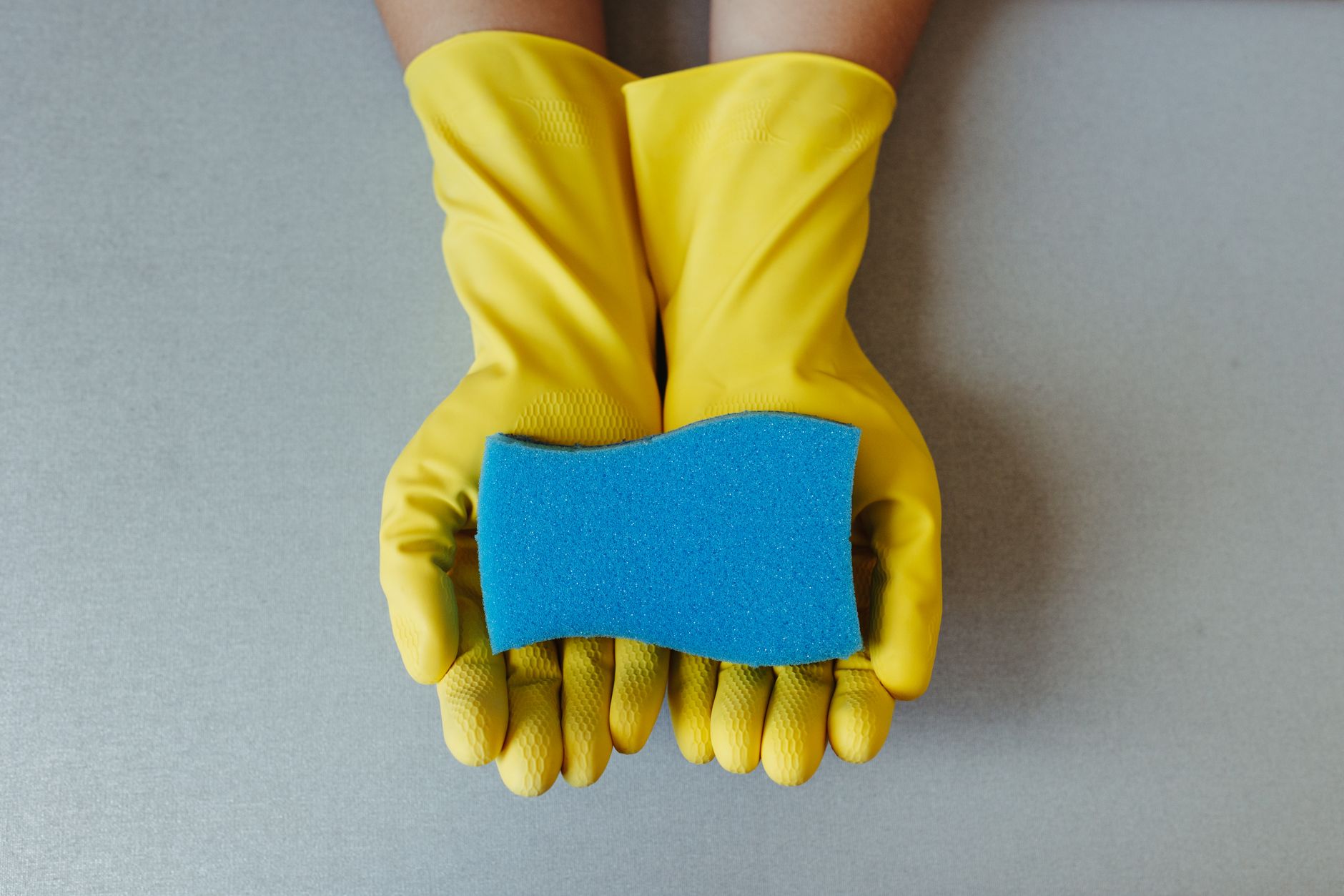 Gants de ménage jaunes tenant une éponge bleue